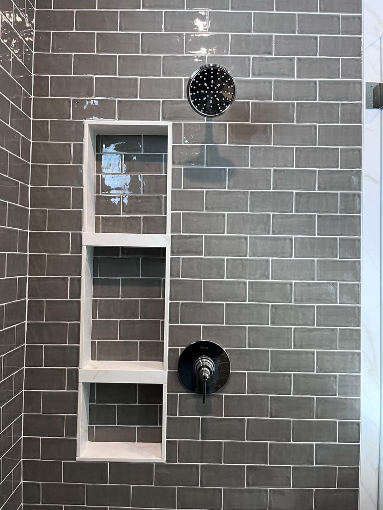 Modern bathroom shower with gray subway tile, built-in shelving niche, black rainfall showerhead, and wall-mounted faucet