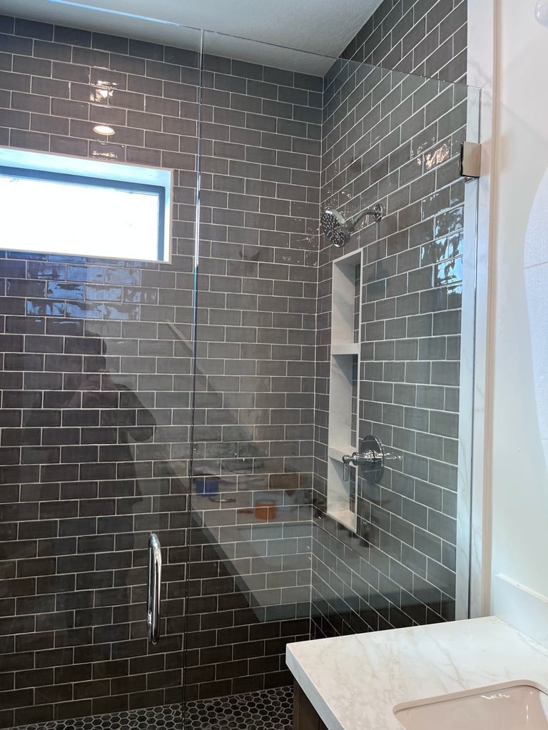 Modern bathroom shower enclosure with dark green subway tile walls, frameless glass door, and built-in shelf niche