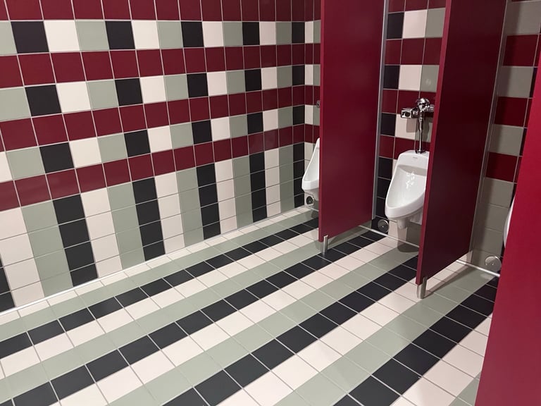 Modern bathroom interior with burgundy and white checkered tile walls and striped black and white floor tile, featuring a white toilet visible through an open door