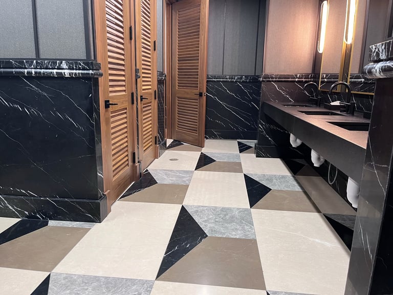 Modern luxury bathroom with black marble walls, geometric diamond-patterned floor in black, white, and gray tiles, wooden louvered doors, and marble sink vanity