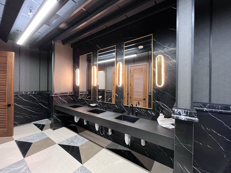 Modern luxury bathroom with black marble countertop, multiple illuminated mirrors, and geometric floor tiles