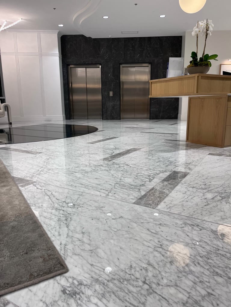 Modern lobby with white marble floor, wooden reception desk, stainless steel elevators, and black marble accent wall
