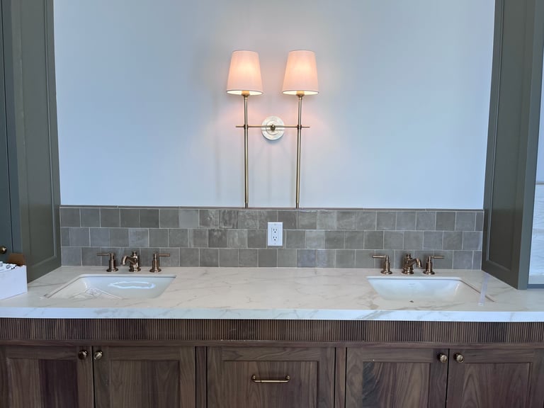 Bathroom vanity with dual sinks, stone countertop, gray tile backsplash, and dual wall sconces above mirrors