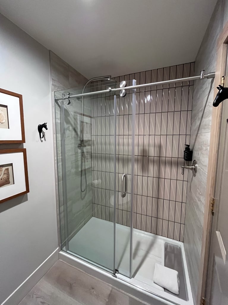 Modern glass-enclosed shower stall with vertical tile walls, sliding glass doors, chrome fixtures, and white towel rack inside bathroom