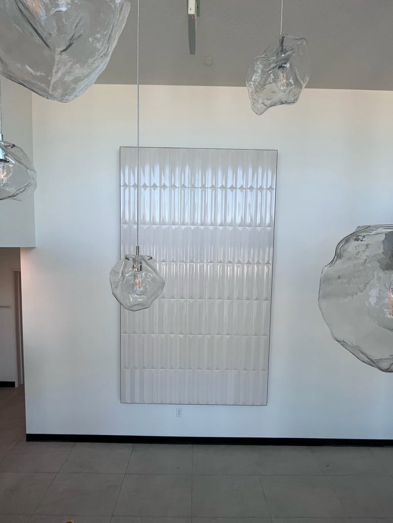 Modern art installation featuring translucent glass pendant lights and a large ribbed panel against a white gallery wall