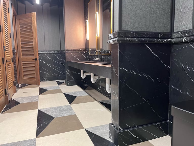 Modern bathroom with geometric black and white floor, marble walls, sleek fixtures, and minimalist design with warm lighting