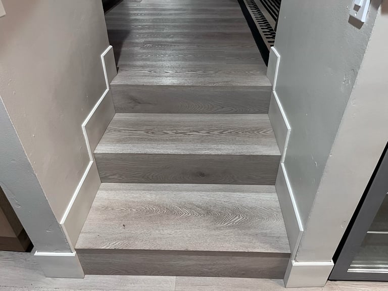 Modern staircase with gray wood-look steps and white illuminated handrails descending into a bright entryway