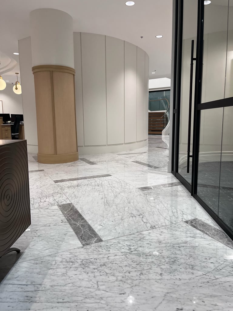 Modern architectural interior with marble flooring, curved beige walls, black-framed glass doors, and recessed lighting